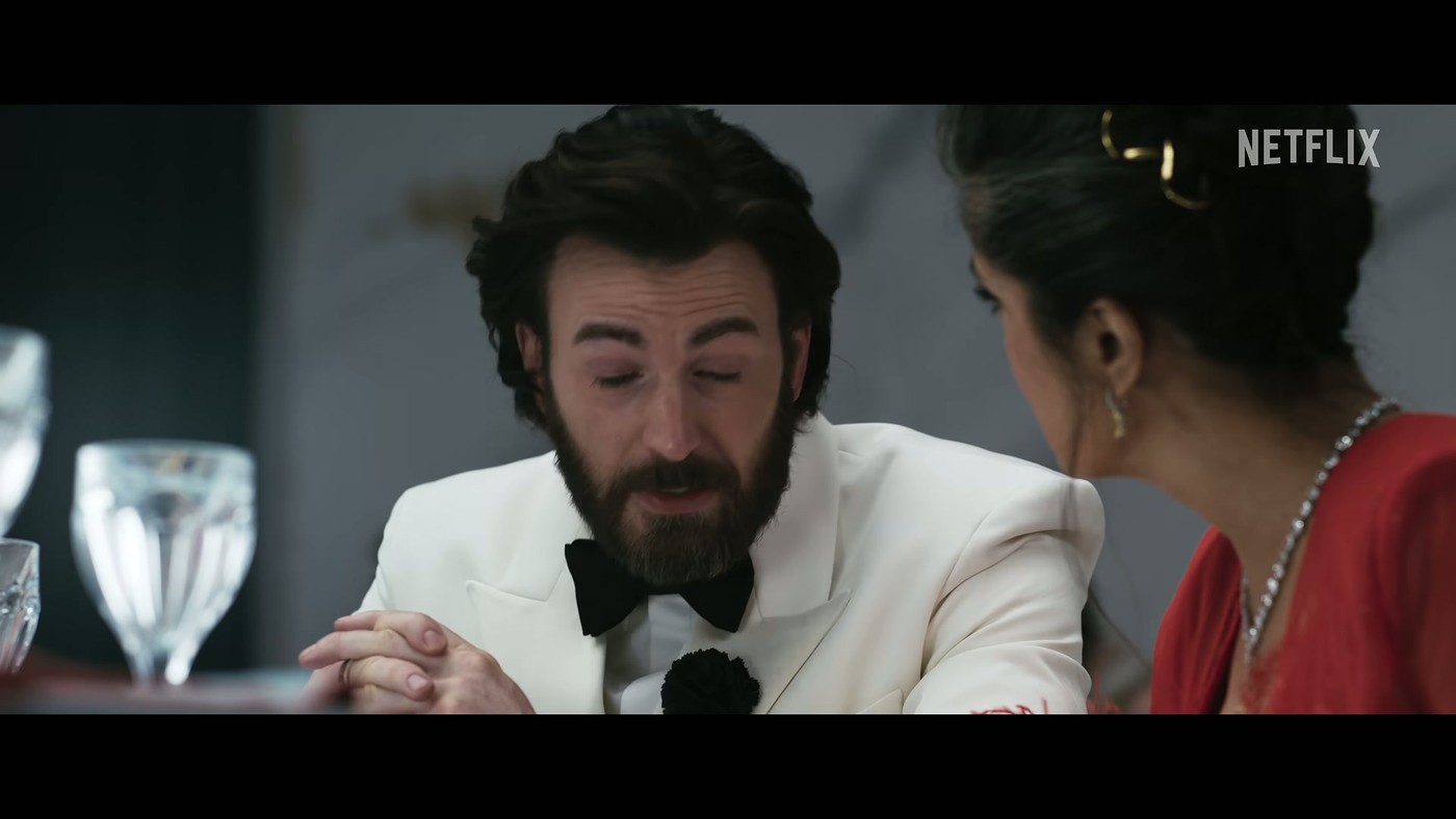 Chris Evans in a white tuxedo at a dinner table in the Sacrifice trailer