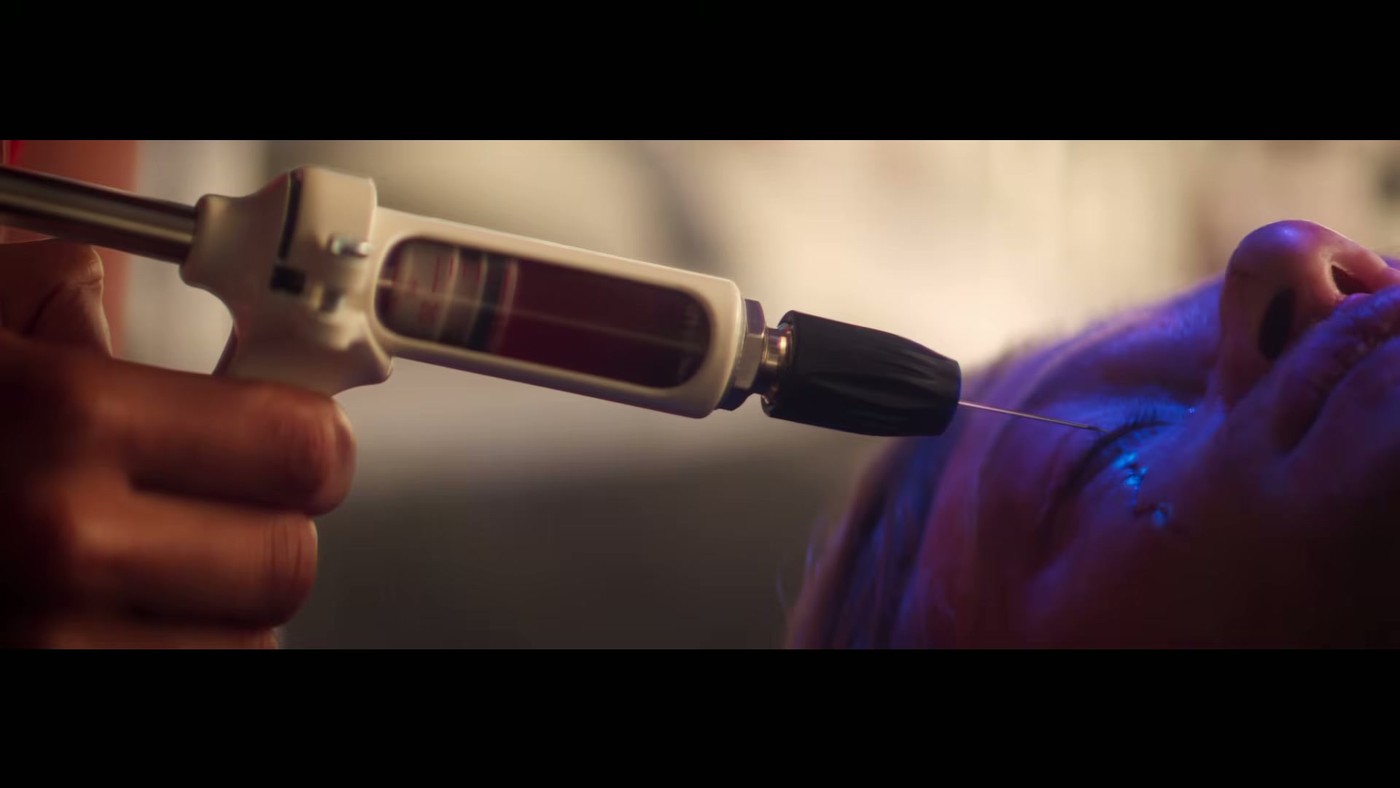 A gloved hand holding a syringe with pink liquid in the Clayface final trailer