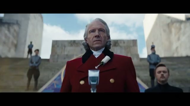 A silver-haired Capitol official in a red coat presides over the reaping ceremony