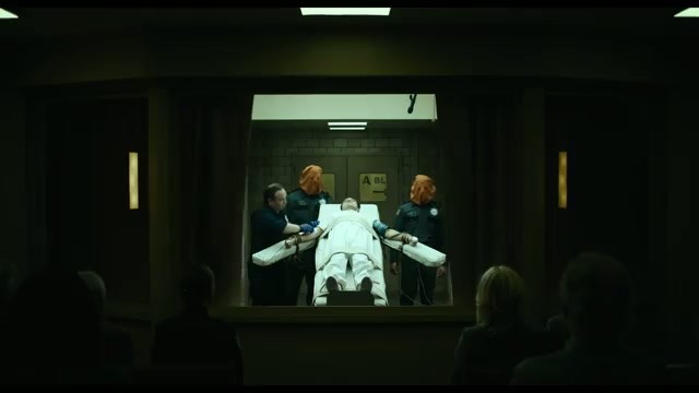 A restrained figure on a gurney in an execution chamber, witnessed through glass